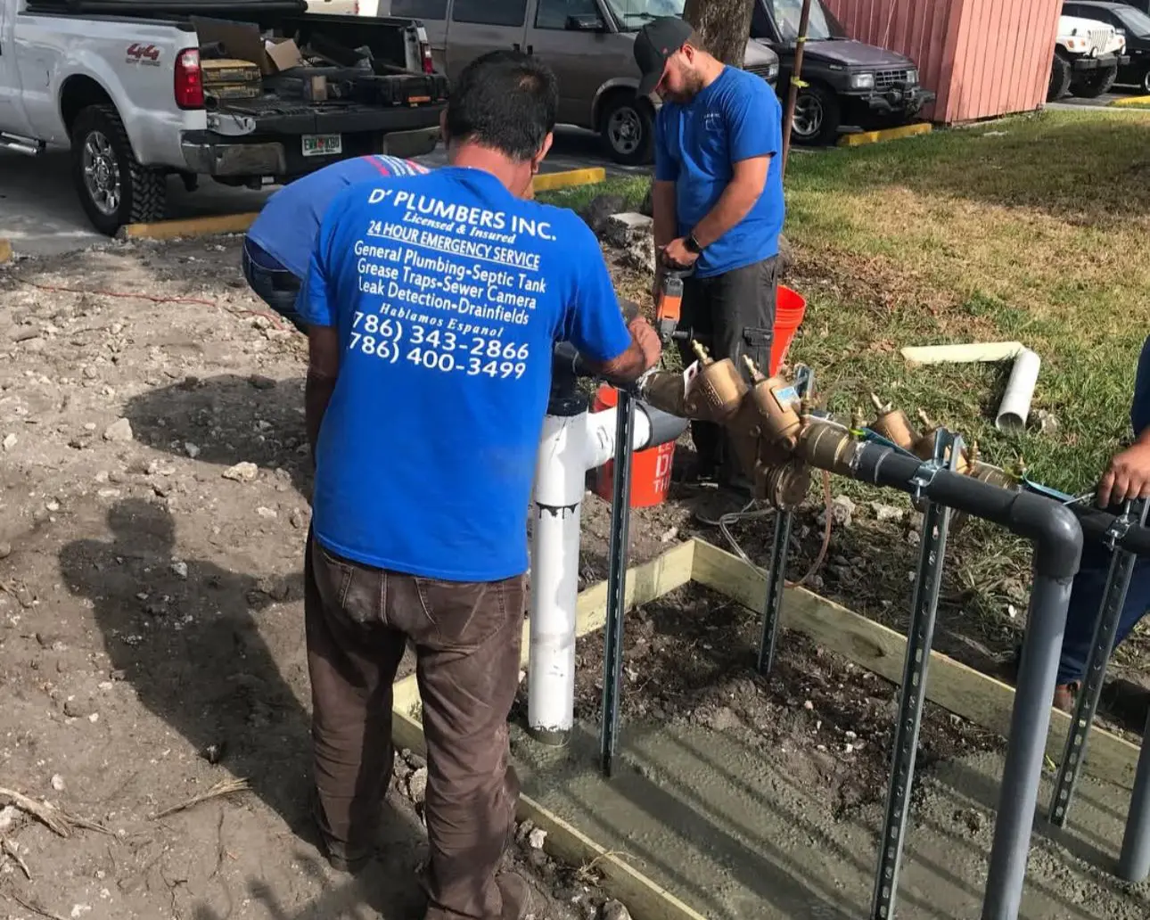 Technicians from D’Plumbers Inc. installing a certified backflow prevention system outdoors, ensuring water supply protection and compliance with plumbing codes.